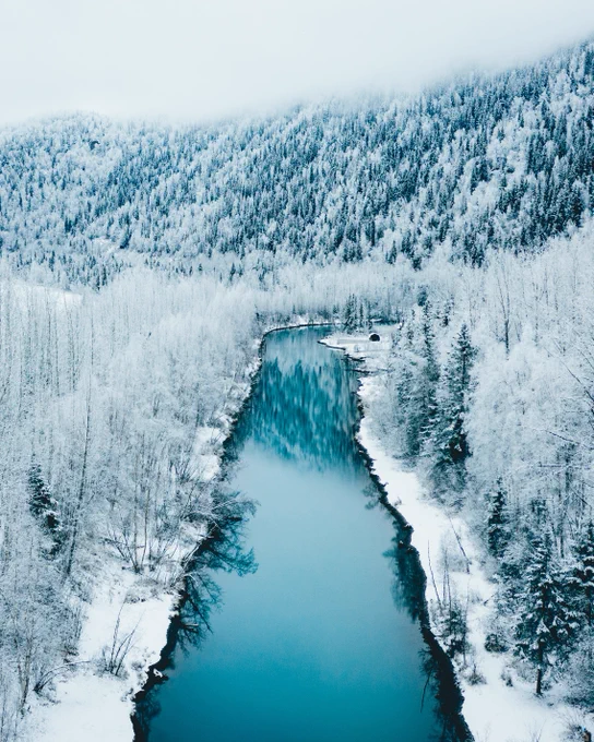 Photo from above of blue river between frosty winter banks. Near Eklutna Tailrace, Eagle River AK. Photo taken by Alaskan photographer, Ellen Carty