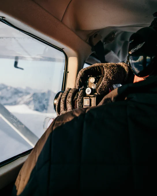 Man taking photo with sony camera out the window of a bush plane in Alaska. Photo taken by Alaskan photographer, Ellen Carty