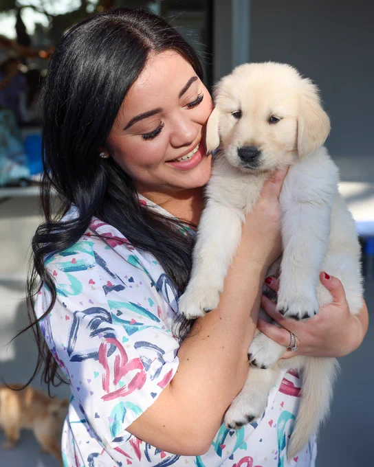 A young woman is smiling while hugging a Golden Retriever puppy. 