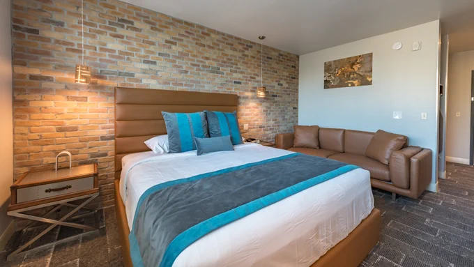 Hotel room at Lexen Hotel North Hollywood with single bed, brick accent wall, night stand, sofa, wall art, hard flooring, hanging lights. 