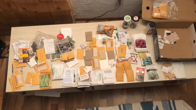 A coffee table covered in various packet, jars, and bag of seeds for the garden.