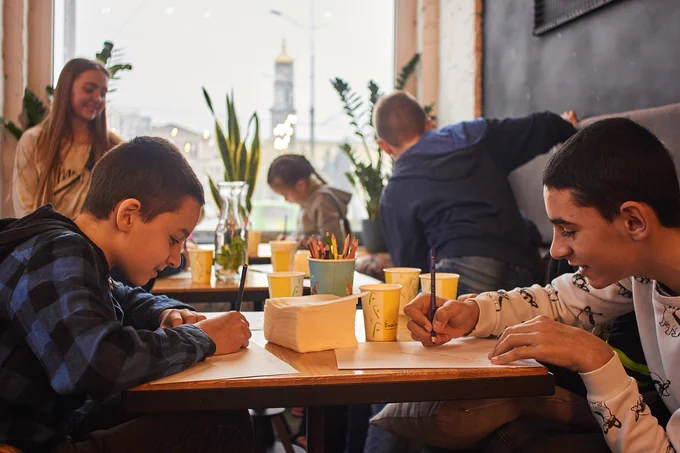 Picture of children sat at a table colouring and drinking hot chocolates.
