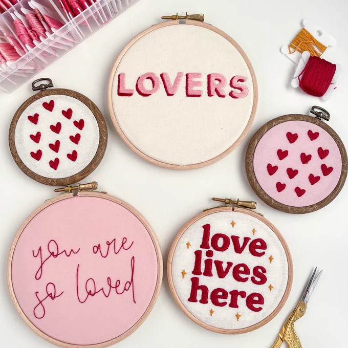5 embroidery hoops with white and pink fabric and hand embroidered red and pink text with hearts and valentines and galentines love quotes. Retro and calligraphy home decor art