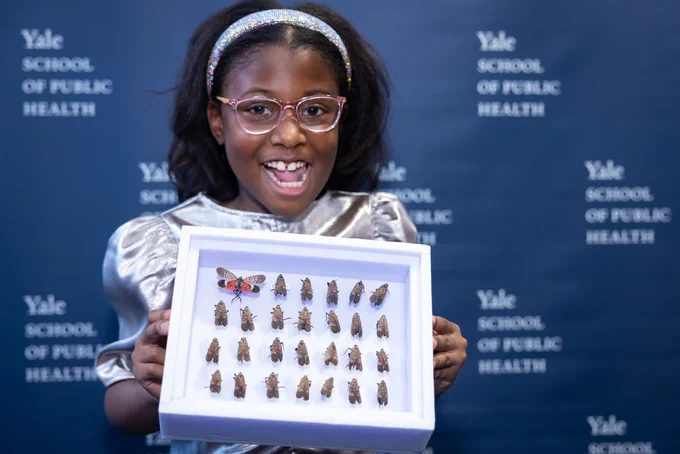 Bobbi Wilson holding framed lanternfly collection in front of Yale School of Public Health backdrop
