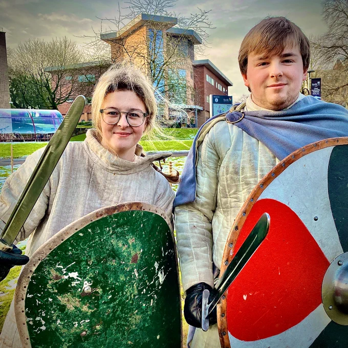 a young girl and man with swords and shields wearing historic outfits.