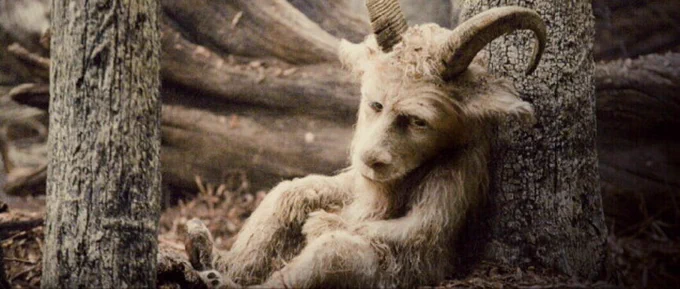 Alexander from Where The Wild Things Are. He is a goat monster with white fur and a human nose. He sits forlornly against a tree.