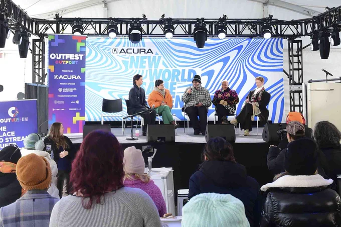 A panel of queer actors sit on the Outfest Outpost stage in front of a crowd.