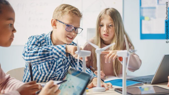 Three kids are observing model energy wind turbines in a school classroom