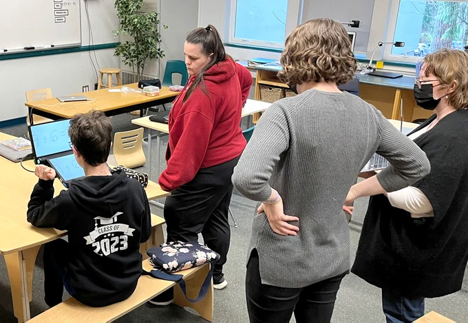 Student working on a low vision device in the the classroom, with the school team assisting him.