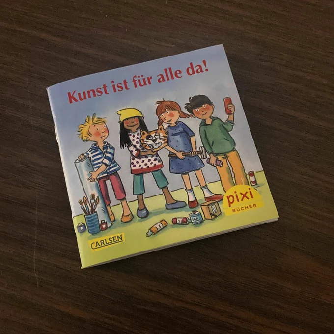 Zu sehen ist ein Pixi-Buch mit dem Titel „Kunst ist für alle da“. Auf dem Cover ist eine Illustration, die vier Kinder und Kunstuntensilien zeigt.