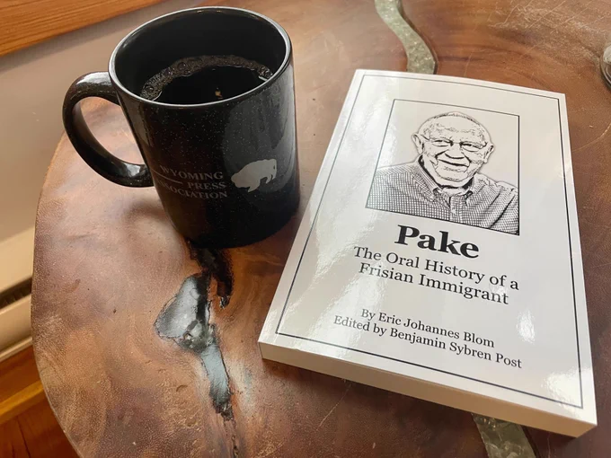 A book called "Pake: The Oral History of a Frisian Immigrant" sits on a table next to a cup of coffee.