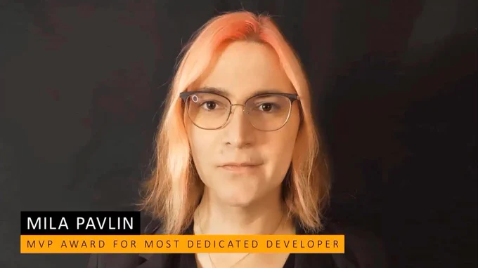 A head shot of Mila facing the camera, with peachy pink hair just reaching her shoulders and glasses. She has only a slight smile. Text reads MVP Award for Most Dedicated Developer.