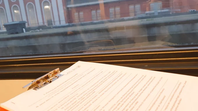 Blick aus dem Zugfenster auf den Bahnhof in Hamm. Im Vordergrund ein Klemmbrett mit dem Programm der 9. Kommunalen Nachhaltigkeitstagung