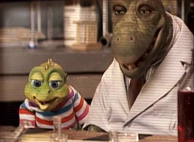 Timmy and Mr. Lizard from Dinosaurs. Timmy is a young, bright green dinosaur in a colourful striped shirt. Mr. Lizard is an older dinosaur in a tie and lab coat. They sit at a lab setting.