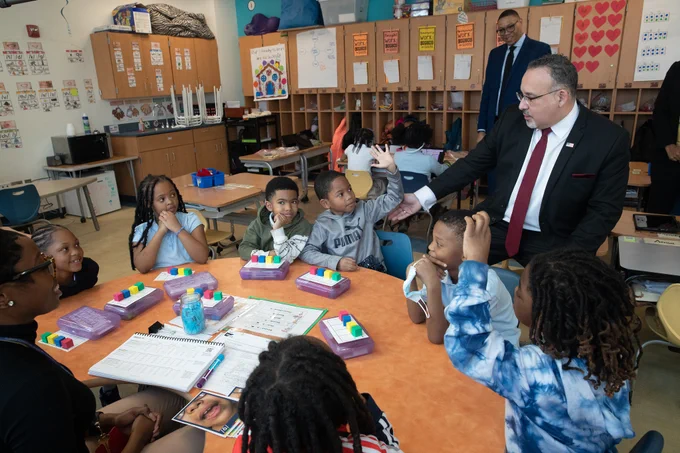 Secretary Cardona sits with a group of students in a classroom during small group discussion. 