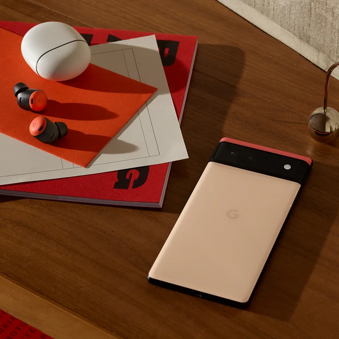 The Pixel Buds Pro in Coral and Google Pixel 6 in Kinda Coral arranged on a wooden table.
