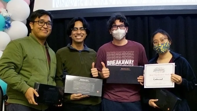 Four TAMU ETID students each holding their paper awards on stage decorated with white and blue balloons. 