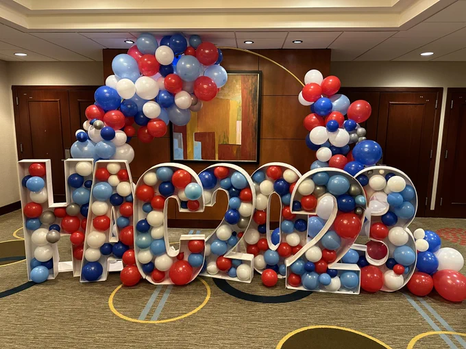 A sign: HAC 2023 festooned with red, blue and white balloons.