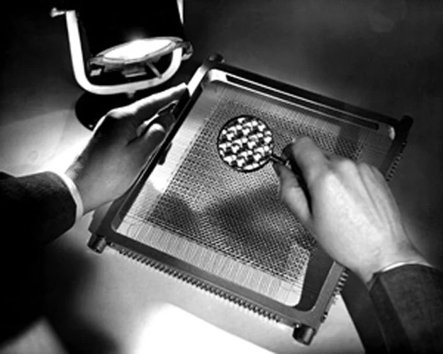 Black and white photo of a person using a magnifying glass to view small toroidal-shaped ferromagnetic cores.