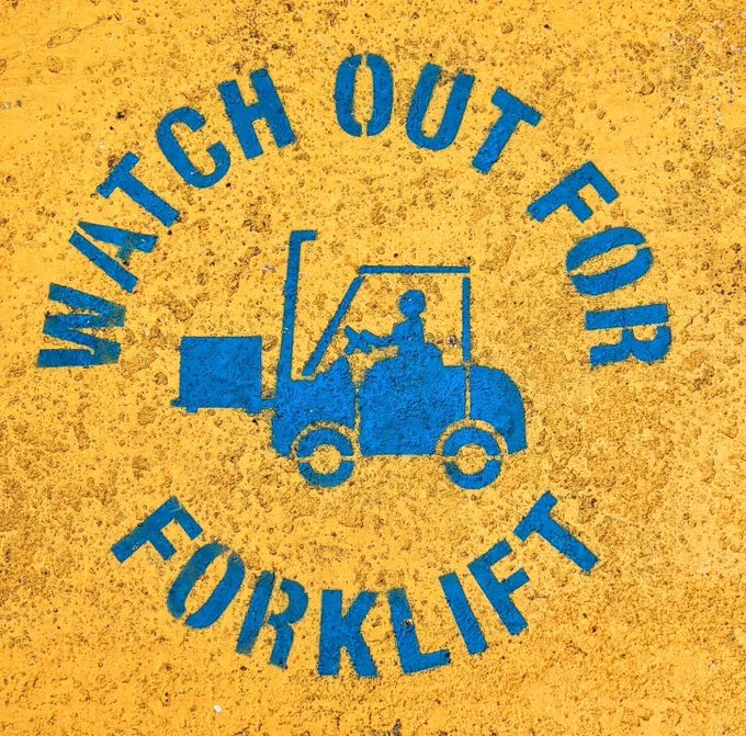 A circular blue stencilled road sign on a yellow background stating "WATCH OUT FOR FORKLIFT", with a picture of a forklift in the middle.