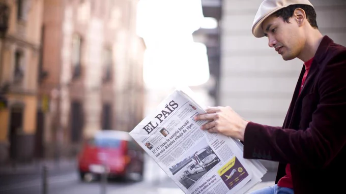 Man sitting outside in a city, looking at a copy of El País, a Spanish national newspaper.