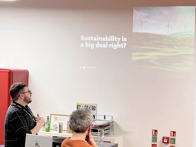 Rick Butterfield on left of picture, looking at his slide which says Sustainability is a big deal right? The picture on the slide is of wind turbines. To the right of Rick us an audience member looking at the slide