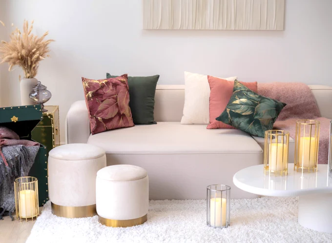 A white couch is in the center of the photo with pink and green pillows, a white carpet and candles on a white table.