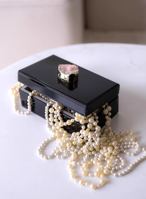 A black jewelry box with a pearl necklace coming out of the box.