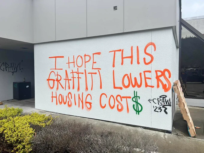 "I hope this graffiti lowers housing cost$" painted on a wall with orange and green spray paint 