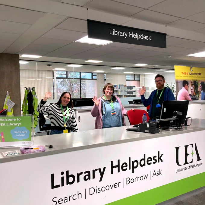 Three helpdesk team members stood behind the Library Helpdesk, smiling and waving. 