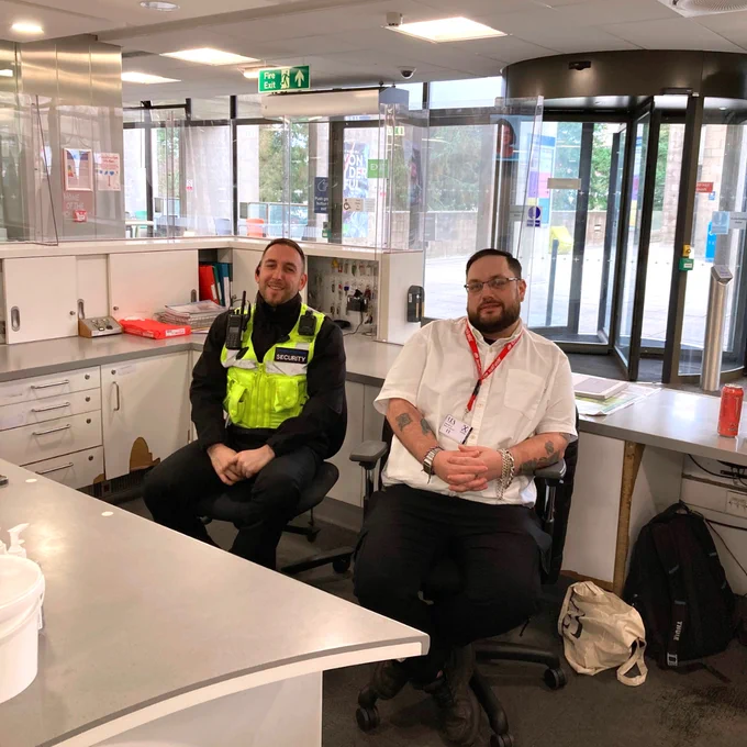 Two security guards at the Library reception desk, smiling.