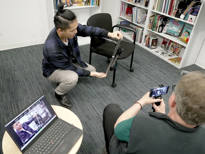 Our OT Wilson securing a mount on a chair while Gary holds up a iphone filming him. Laptop on the left displays the live capture.