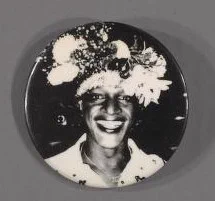 A pin made of a black and white portrait of Marsha P. Johnson in a floral crown. 
