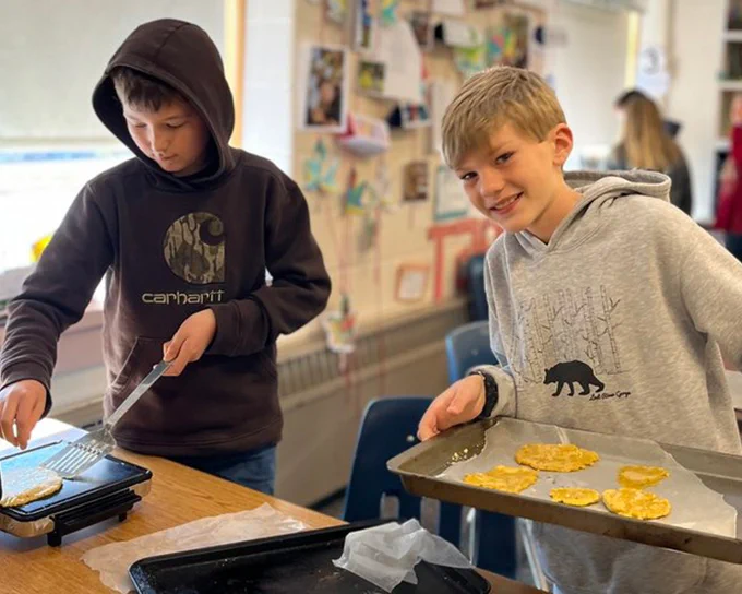 Two students cook homemade tortillas in the classroom.
