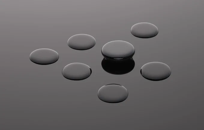 Seven circular, domed glass faces of the Google Pixel Watch arranged on a gray surface. One of the faces is raised above the surface, revealing a portion of the watch below.