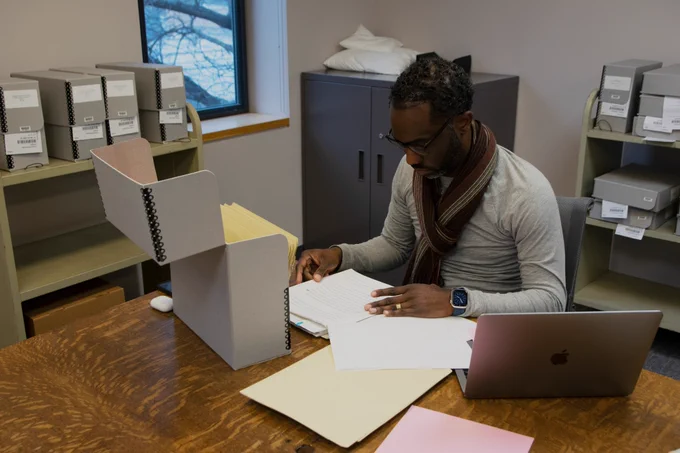 Professor Joseph Tucker Edmonds reads the Pearson papers. A large, grey Hollinger box with Pearson's papers stands open on the table.