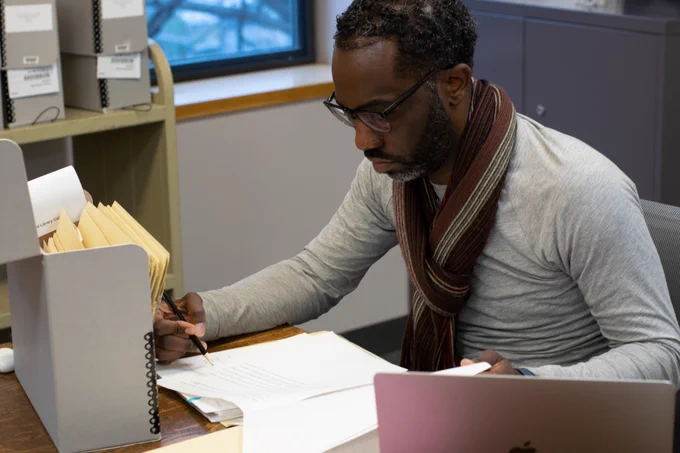 Professor Joseph Tucker Edmonds studies the Carlton Pearson papers. He wears a red scarf over a grey shirt.