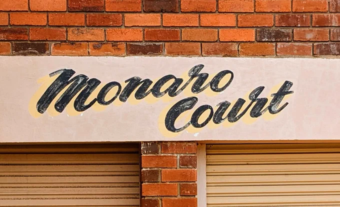 A faded, hand painted sign on a block of flats called "Monaro Court"
