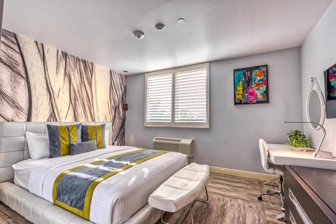 Lexen Hotel North Hollywood Room with Single platform bed, bright colored pillows and bed scarf, bright wall art, desk, chair, lamp, black and white palm tree accent wall.