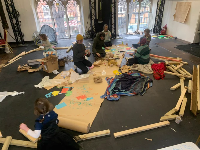 A group of parents/children play with timber to create a nest.