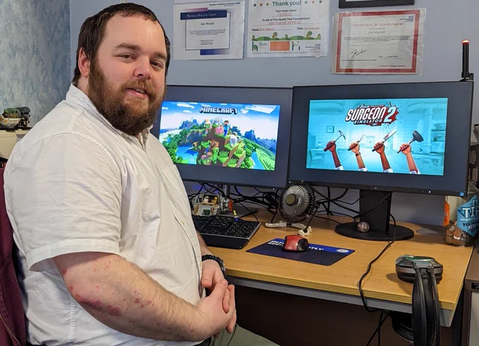 A man sat in front of two computer screens showing Minecraft and Surgeon Simulator 2.