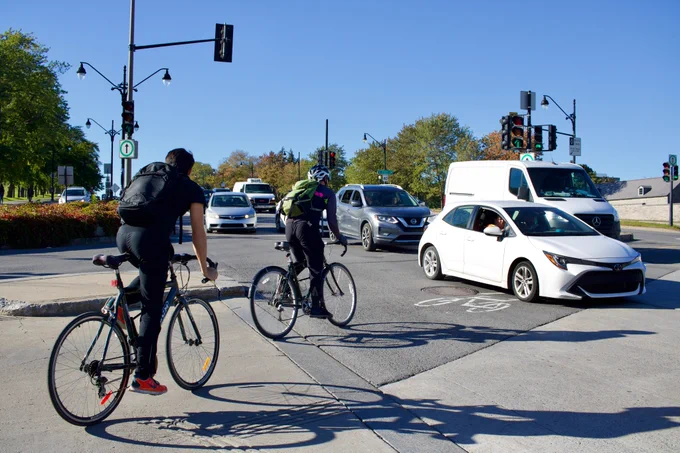 Two people biking through a row of vehicles despite a green light for cyclists