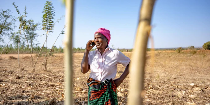 African women farmer standing in a field talking on a cellphone