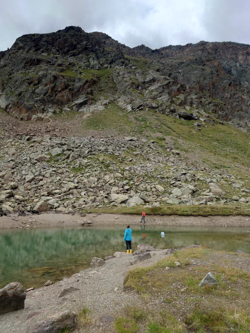 Mountain lake with two people on both sides of the water, holding ropes to a floating box on the water. 