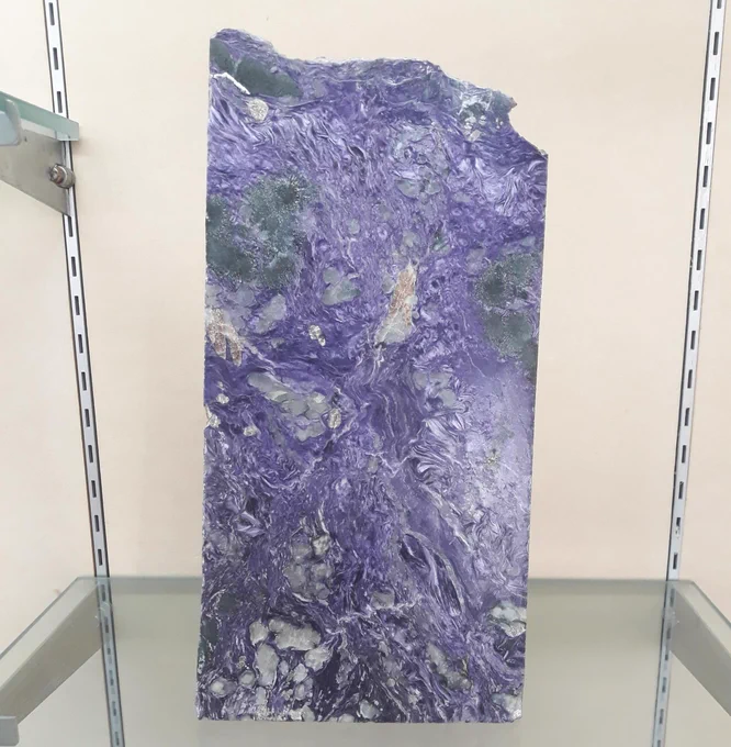 A large polished slab of charoite which consists of swirling patterns of white and deep purple, with larger patches of white, black and orange.