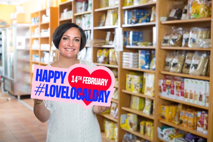 Image depicts a shopkeeper holding a sign which reads ‘Happy #LoveLocalDay 14TH February’