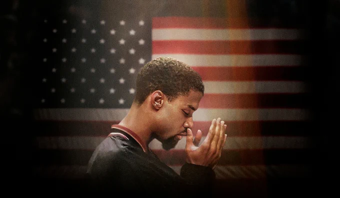 Mahmoud Abdul-Rauf holds his hands in prayer in front of the USA flag while wearing a Denver Nuggets warmup jacket