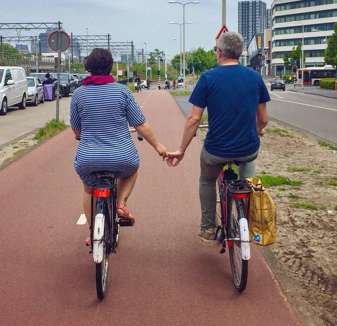 Melissa and Chris Bruntlett of @modacitylife riding hand in hand along a bike path