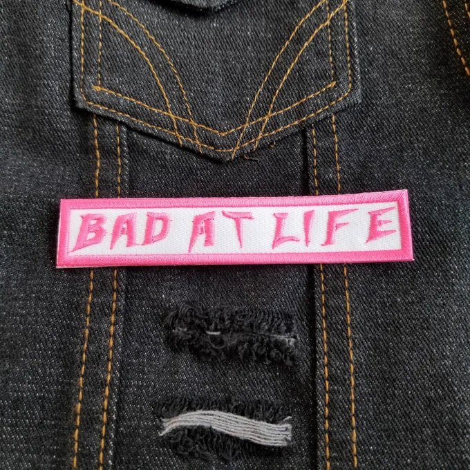 Bad at life embroidered patch in pink on white.