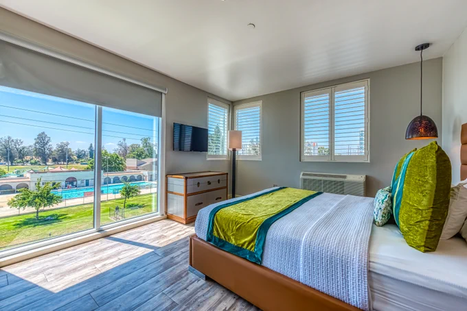 Lexen Hotel North Hollywood Room with bed, TV, dresser, pendant light, windows showcase blue skies and greenery.